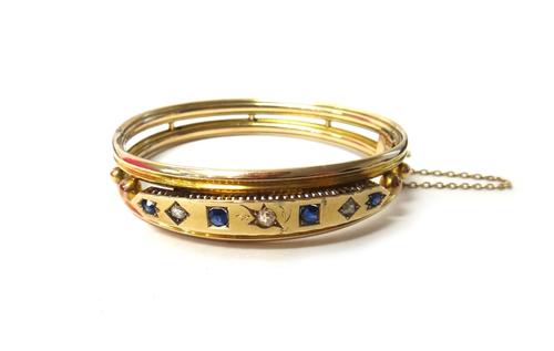 A sapphire and diamond set oval hinged bangle, with the principle cushion shaped diamond mounted at the centre, between two pairs of cushion shape sap