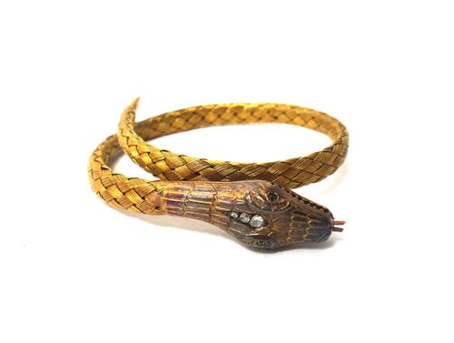 A gold and diamond set bracelet, designed as a coiled snake, the snake's head mounted with a row of three rose cut diamonds and with emerald set eyes,