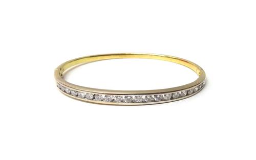 A gold and diamond set oval hinged bangle, mounted with a row of twenty circular cut diamonds graduating in size to the centre stone, on a snap clasp