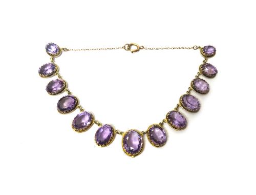 A silver gilt and amethyst necklace, claw set with a row of thirteen oval cut amethysts graduating in size to the front, on an oval link neckchain, ha