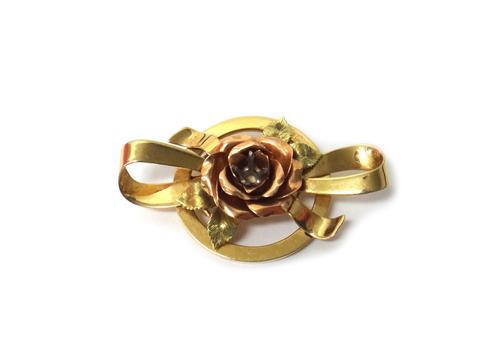 A two colour gold brooch, designed as a central flowerhead, two pairs of leaves and a bow (the central gemstone lacking), detailed 14 K, weight 16.8 g