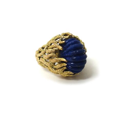 A gold ring, claw set with an oval ridged lapis lazuli, the mount in a cast and pierced marine foliate design, ring size M, gross weight 18gms.