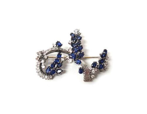 A white gold, sapphire and diamond set brooch, in a scrolling open work design, mounted with circular cut and baguette diamonds and with pear shaped s
