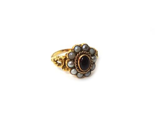 A gold, carbuncle garnet and seed pearl set oval cluster ring, mounted with the oval carbuncle garnet at the centre, in a surround of seed pearls, bet