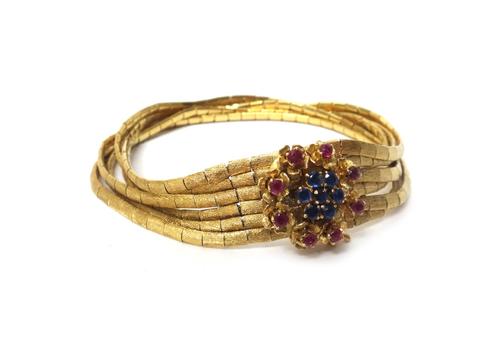 A gold, sapphire and ruby set bracelet, designed as six rows of baton shaped links, having a textured finish, on a sapphire and diamond set cluster cl