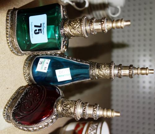 Three Middle Eastern coloured glass and white metal mounted perfume bottle atomisers, 20th century, each of shaped form, the tallest 16.5cm high. (3)