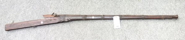 A crude wooden rifle, 19th century, with circular steel barrel 119cm and carved wooden body, the barrel bound with a leather strapping, 173cm overall.