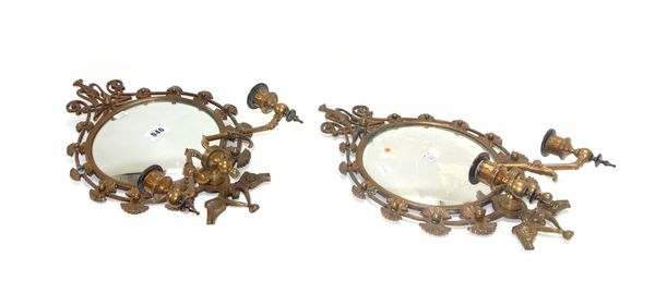 A pair of patinated brass mirror wall sconces of Aesthetic Movement style, the concave plate with a foliate cast pierced border issuing two adjustable