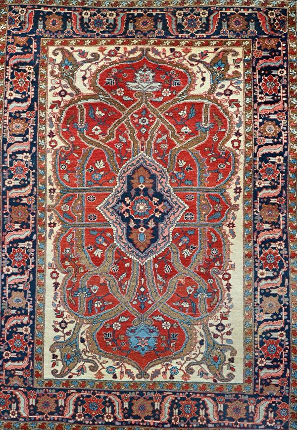 A Heriz carpet, Persian, the shaped madder field with an indigo medallion, brown ribbon design; with ivory spandrels; an indigo flowerhead, leaf and v