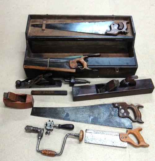 An early 20th century black painted pine tool box containing carpenters tools, saws, planes, hand drills and sundry, (qty).  L7