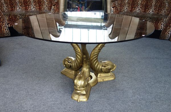 A 20th century dining table, the circular smoked glass top on three lacquered brass dolphin supports, 143cm wide.