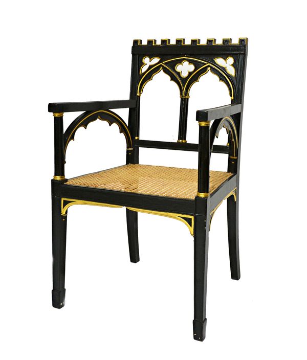 A Regency Gothic Revival ebonised parcel gilt open armchair, with castellated arch back and cane seat, 53cm wide x 92cm high.   Illustrated