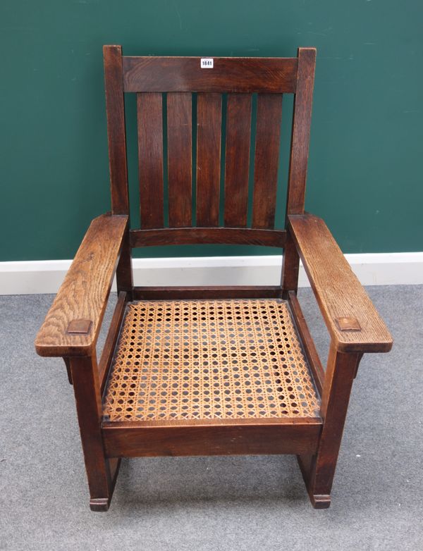 An early 20th century oak rocking chair in the manner of Gustav Stickley, with five slat back above broad arms with projecting tenons, on a plain rock