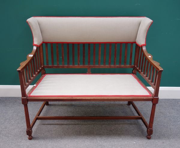 An Edwardian mahogany wingback small settee, with padded top rail above slat filled back and arms, the padded seat on turned tapering legs united by s