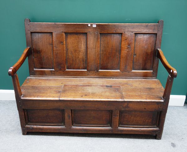 An 18th century oak four panel back open arm box settle, on canted square supports, 136cm wide x 103cm high.