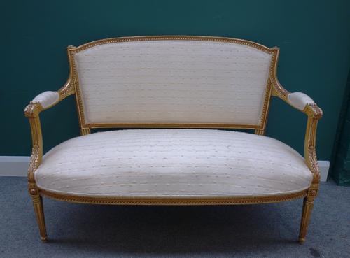A Louis XVI style gilt framed open arm sofa, with bow seat on tapering fluted supports, 130cm wide x 93cm high.