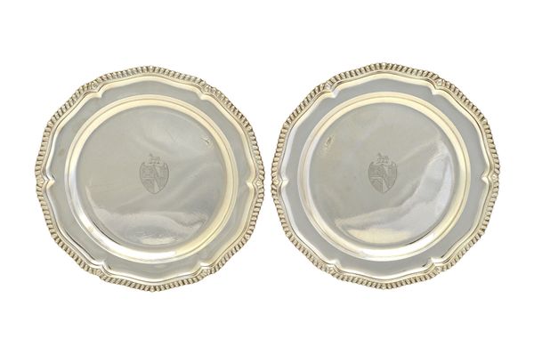 A pair of George III silver main course plates, each of shaped circular form, engraved with a shield and a crest to the centre, within a gadrooned rim