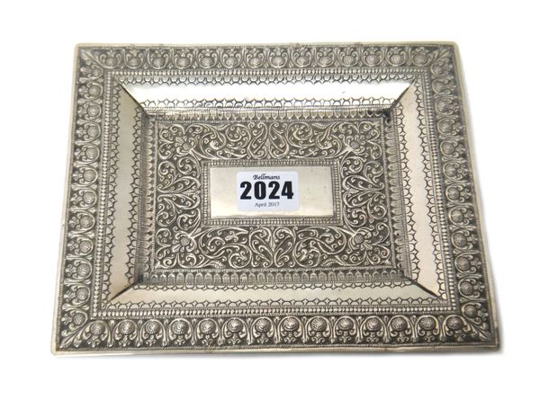 A Middle Eastern rectangular white metal dish, with a vacant central rectangular panel within a bold scrolling foliate border and with a wide decorate