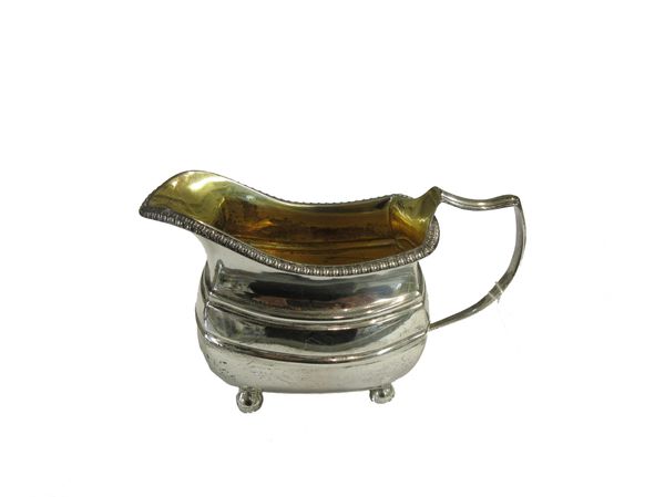 A George III silver milk jug, of curved rectangular form, decorated with a gadrooned rim and raised on four spherical feet, London 1812, weight 188 gm