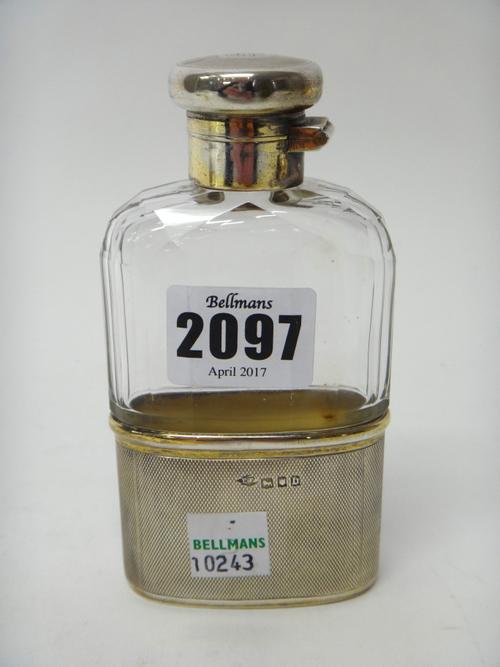 A silver mounted, faceted glass spirit flask, formerly gilt, with engine turned decoration and with a pull-off beaker base, London 1917, the hinged co