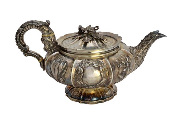 A George IV silver teapot, of compressed circular form, the body with floral and wreath motifs to the panels, the hinged lid with a cast flower finial