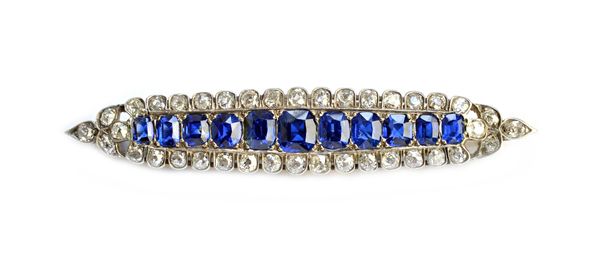 A sapphire and diamond brooch, of shallow oval form, mounted to the centre with a row of eleven cushion shaped sapphires, graduating in size to the ce