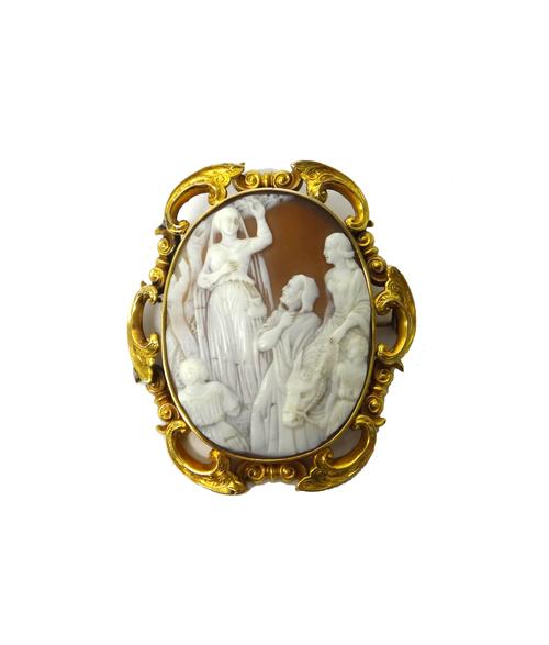 A Victorian gold mounted oval shell cameo brooch, carved as The Flight into Egypt, the mount decorated with a scrolling border and with engraved decor