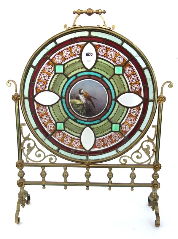A Victorian brass and glass mounted fire screen of Gothic style, the circular frame inset with a coloured glass panel centred with a wild bird, 79cm h