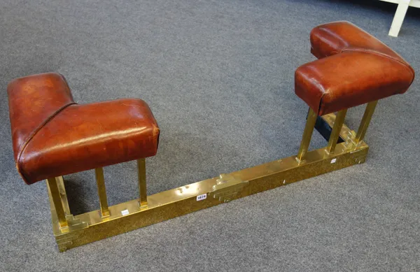 An Art Deco brass and leather upholstered club fender, the square pillars over a square base with raised Art Deco embellishments, 111cm wide.
