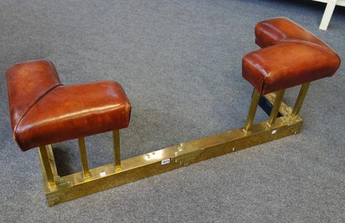 An Art Deco brass and leather upholstered club fender, the square pillars over a square base with raised Art Deco embellishments, 111cm wide.