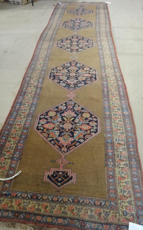 A Bidjar runner, Persian, the plain brown field with five dark indigo herate pattern medallions, three borders, 437cm x 117cm.