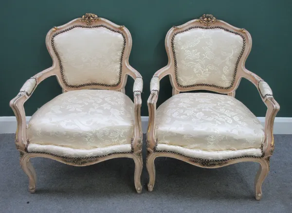 A pair of Louis XV style cream painted parcel gilt open armchairs, with serpentine seats and scroll supports, 68cm wide x 92cm high.