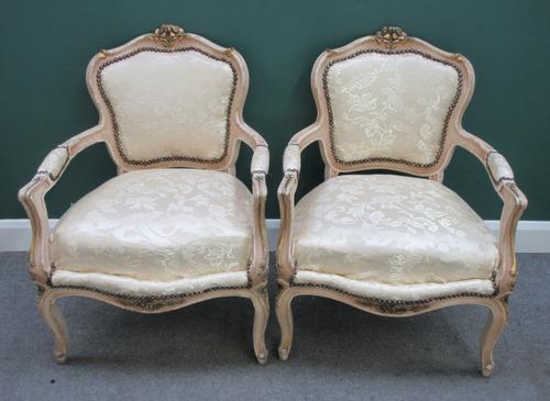 A pair of Louis XV style cream painted parcel gilt open armchairs, with serpentine seats and scroll supports, 68cm wide x 92cm high.