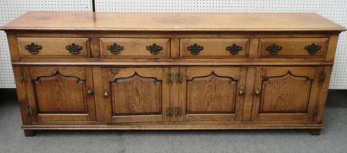 An 18th century style oak dresser base, with four drawers over four arched panel cupboards, on stile feet, 230cm wide x 86cm high x 50cm deep.