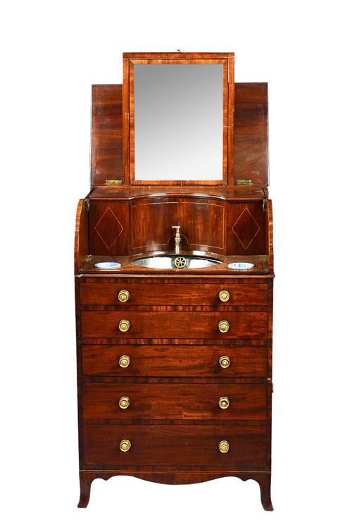 An early 19th century inlaid mahogany cylinder fronted washstand, the lift top enclosing a fitted interior with mirror basin and reservoir over four d