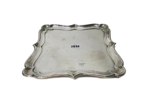 A silver salver, of shaped square form, with a pie-crust rim, in the early 18th century taste, raised on four scrolled corner feet, width 27cm, weight
