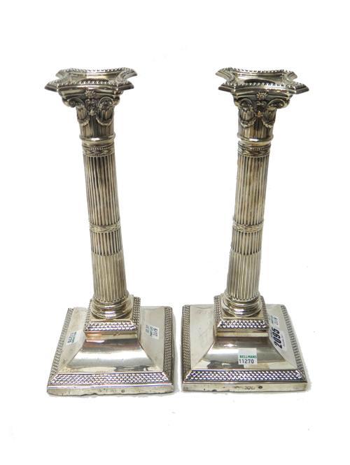 A pair of silver table candlesticks, each formed as a Classical column, with fluted decoration and raised on a square base decorated with a scaling bo