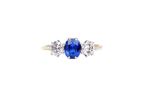 A gold, sapphire and diamond set three stone ring, claw set with an oval cut sapphire at the centre, between two circular cut diamonds, detailed 18 CT