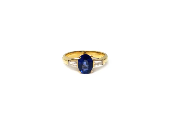 A gold, sapphire and diamond three stone ring, claw set with the oval cut sapphire at the centre, between tapered baguette diamond set single stone sh