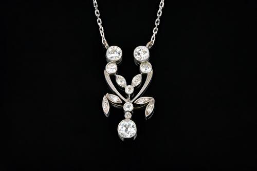A diamond pendant necklace, the front in an openwork foliate design, collet set with the principle cushion shaped diamond to the pendant drop and furt