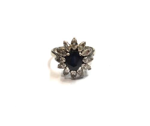 A gold and platinum, sapphire and diamond set flowerhead shaped cluster ring, claw set with the oval cut sapphire in a surround of twelve marquise sha