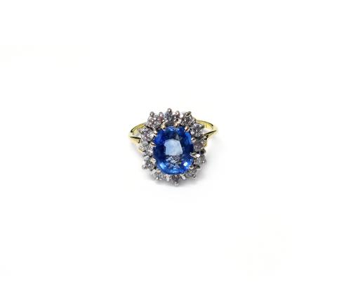 An 18ct gold, sapphire and diamond set oval cluster ring, claw set with the cushion shaped Ceylon sapphire at the centre, in a surround of twelve circ