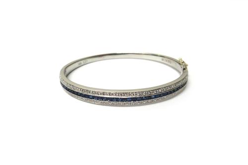 A white gold, sapphire and diamond set oval hinged bangle, the front mounted with a row of calibre cut sapphires to the centre and with a row of circu