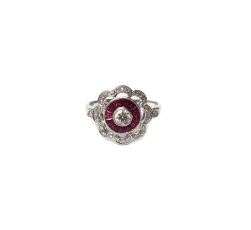 A white gold, diamond and ruby set shaped circular cluster ring, collet set with the principal circular cut diamond at the centre, in a surround of ca