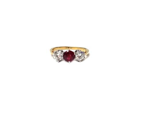 An 18ct gold, ruby and diamond set three stone ring, claw set with the circular cut ruby at the centre, between two circular cut diamonds, detailed 18