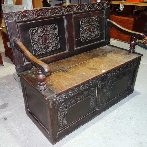 A carved oak bench, incorporating 17th century and later timber, twin panel back above shaped arms with hinged open set, above wave and lunette carved