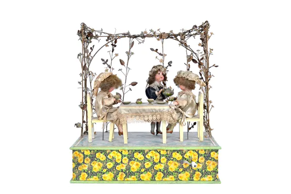 A French bisque doll automaton, late 19th century, depicting three small dolls taking tea, seating at a dining table beneath a floral bocage on a rect