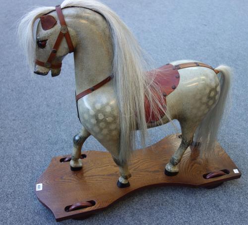 A child's dapple grey ride-on horse, 20th century, with leather saddlery, on an oak plinth and four wheels, 74cm high.