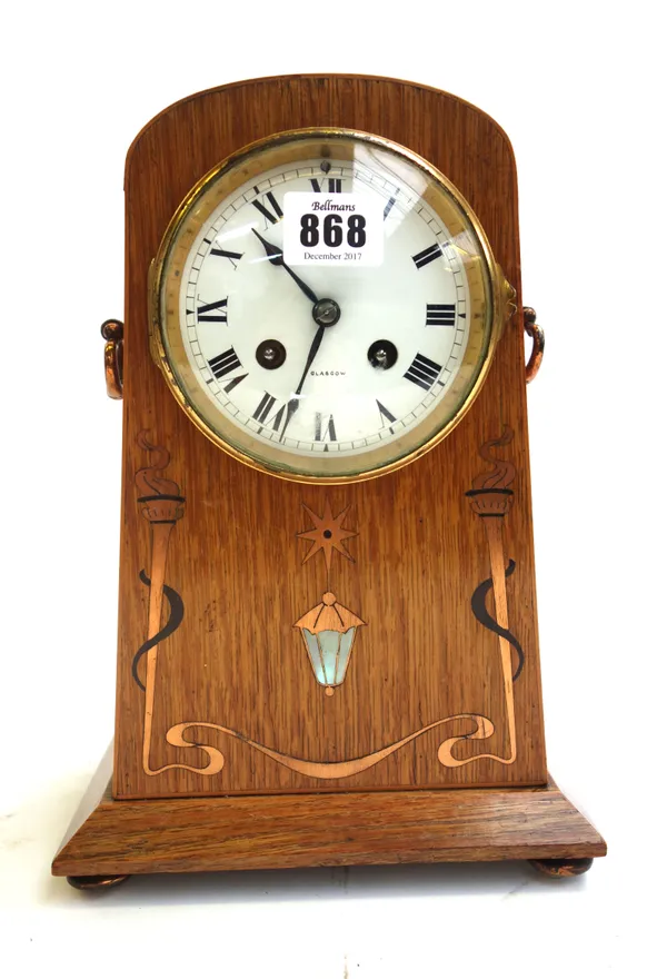 An oak Arts and Crafts mantel clock, with copper and mother-of-pearl inlay, the twin handles flanking an enamelled dial detailed 'Sorley Glasgow', enc
