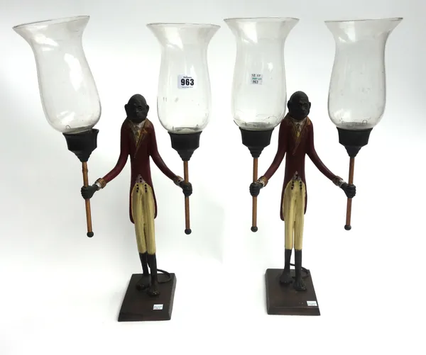 A pair of modern polychrome painted metal two branch candelabra, modelled as a suited monkey, each holding a torch with glass hurricane shades (55cm h